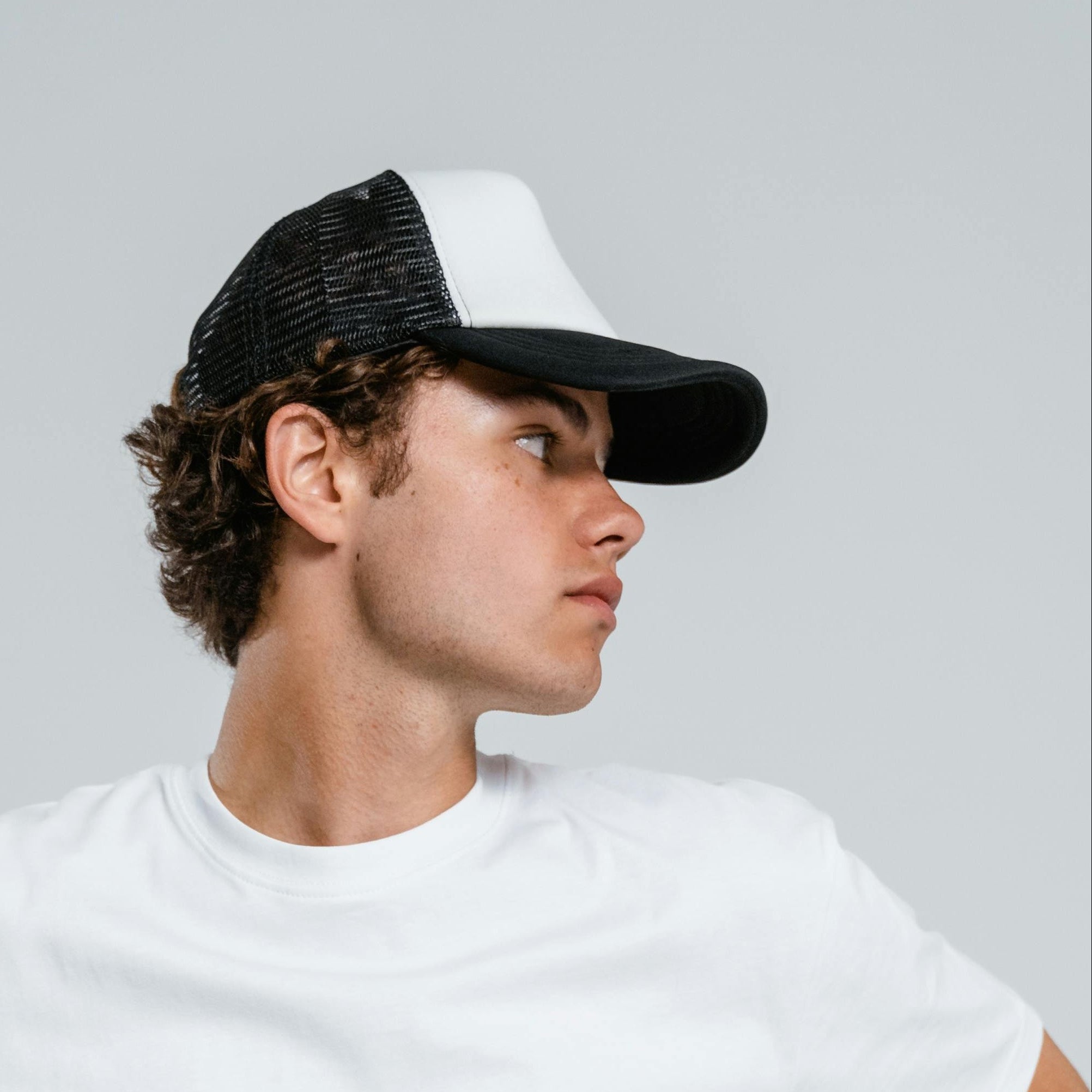 Person wearing a white t-shirt and black cap on a gray background